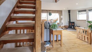 A wooden staircase leading to a loft bedroom with a skylight, a cozy living area with a fireplace, and a dining table with a plant. - The Hayloft (Abergele)