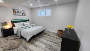 A bedroom with a bed, bedside tables, a nightstand, a window, and a small desk with a vase of flowers. - Welcome to Sunny’s Homes! This spacious upper-level unit in West Edmonton. (Edmonton)
