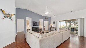 A spacious living room with a large sofa, a fireplace, a ceiling fan, and a view through large sliding glass doors. - Villa S&G: Spacious 5 bedroom, family vacations (Inverness)