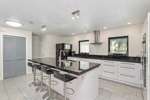 A modern kitchen with a central island, bar stools, stainless steel appliances, and a window providing a view. - Soak Up the Sun: 3BR Pool & Jacuzzi Home Near Inverness (Inverness)