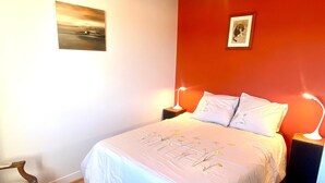 Ein Schlafzimmer mit einem großen Bett, zwei Nachttischlampen, einem Sessel und zwei gerahmten Bildern an den Wänden.