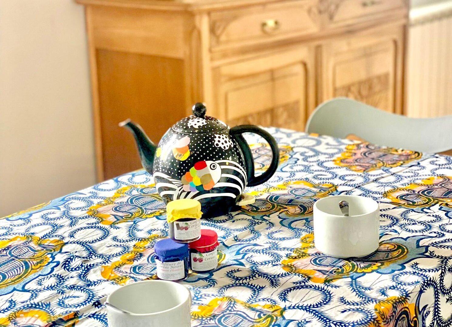 Una mesa con mantel estampado, una tetera decorativa y dos tazas.