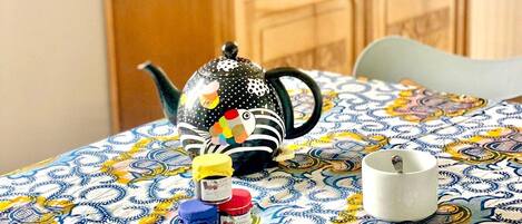 Una mesa con mantel estampado, una tetera decorativa y dos tazas.