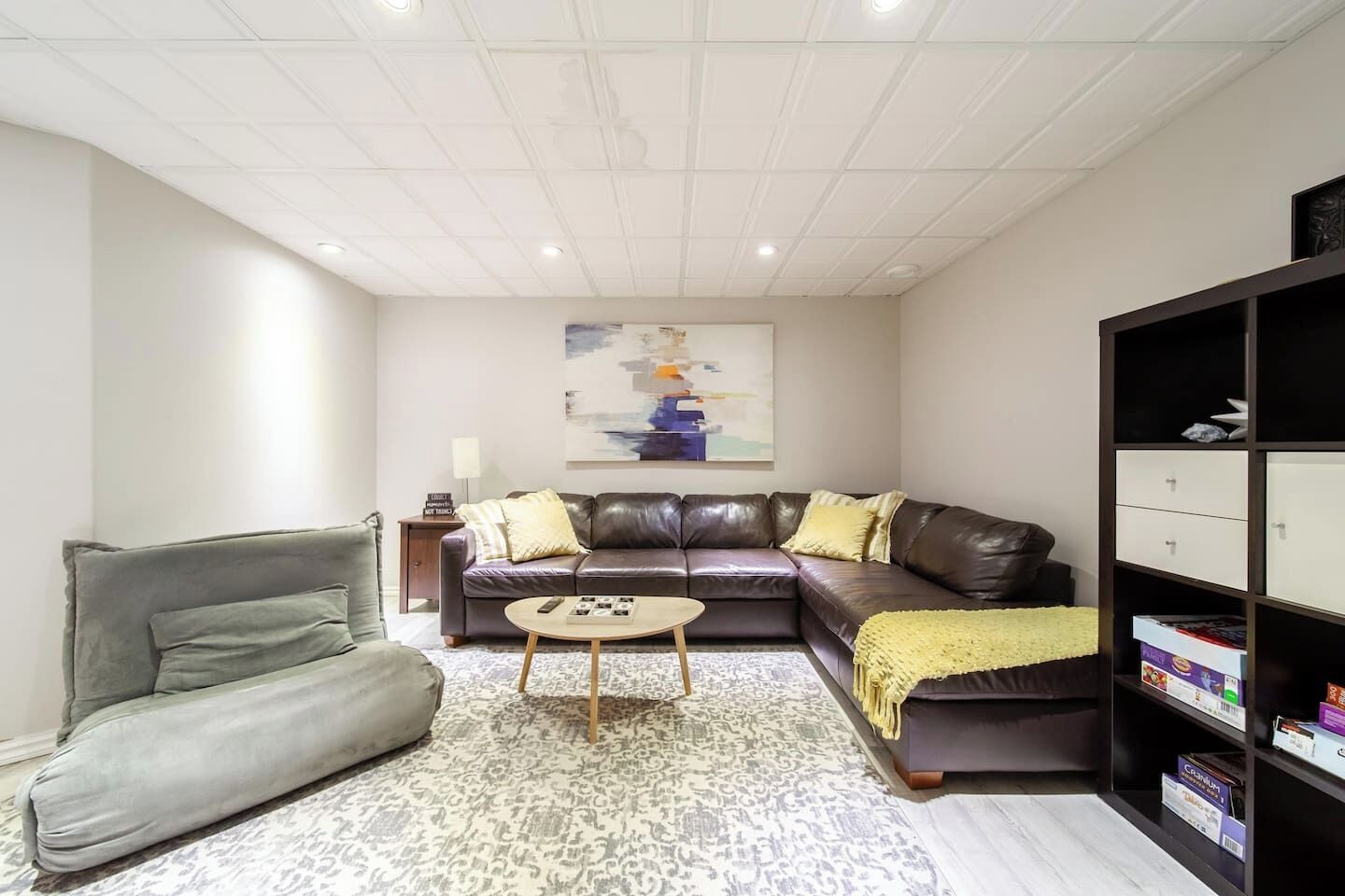 Een moderne woonkamer met een leren bank, een grijze fauteuil, een salontafel en een boekenkast.