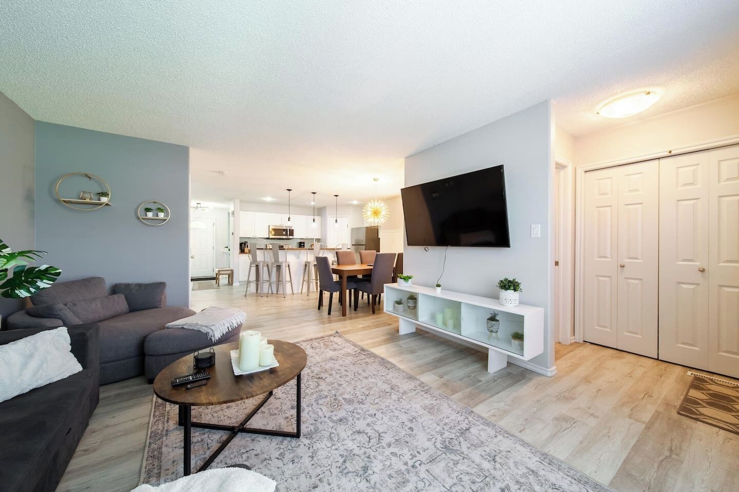 A modern living room with a sofa, coffee table, and TV. There is a dining area with chairs and a table in the background.