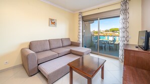A living room with a sofa, a coffee table, a TV, and a sliding glass door leading to an outdoor area. - 1-Bedroom Apartment with Garden View, Shared Pool, Wi-Fi & Air Conditioning (Porches)