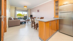 A modern kitchen with wooden cabinets, a built-in refrigerator, and a dining area with a table and chairs. - 1-Bedroom Apartment with Garden View, Shared Pool, Wi-Fi & Air Conditioning (Porches)