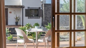Eine geöffnete Tür, die zu einer Terrasse mit weißem Tisch und Stühlen, einem Blumentopf und einem Haus mit Steinmauer und Fensterläden führt.