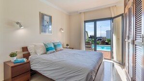 Ein Schlafzimmer mit Bett, Nachttischen, einem Gemälde und Blick auf einen Pool.
