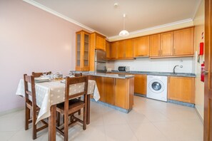 Une cuisine compacte avec des meubles en bois, un lave-linge encastré et un coin repas avec une table dressée pour deux personnes.