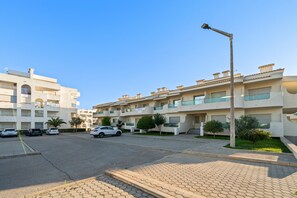 Un immeuble résidentiel doté de nombreux balcons, d’une allée pavée et de voitures garées.