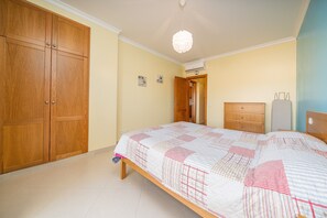 Une chambre à coucher comprenant un lit, une armoire en bois, une commode et un luminaire suspendu.