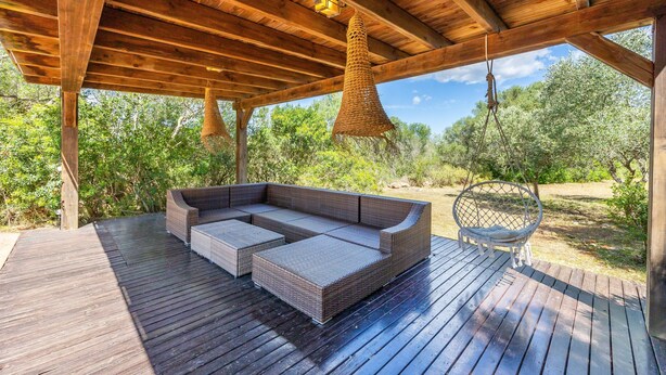Eine Holzterrasse mit Ecksofa und einer Hängematte, umgeben von viel Grün.