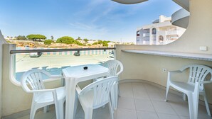 Varanda com cadeiras de plástico branco e uma pequena mesa, com vista para uma área residencial com casas e árvores.