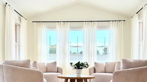 A spacious room with a wooden floor, a round table with a plant, two beige armchairs, and a ceiling fan. - Spacious 5-Bedroom House with Pool and Hot Tub for Families & Groups (Dundee)