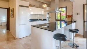 A modern kitchen with a central island, bar stools, and a view of the outdoors. - Holiday Home 'S'altra Casa' with Private Pool, Wi-Fi & Air Conditioning (Illes Balears)