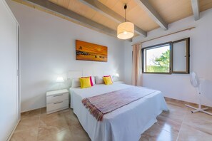 Een slaapkamer met een bed, nachtkastjes, een raam met gordijnen en een schilderij aan de muur.
