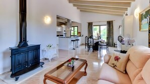 A modern living room with a black wood-burning stove, a glass coffee table, a beige sofa, and a dining area with a white table and chairs. - Holiday Home 'S'altra Casa' with Private Pool, Wi-Fi & Air Conditioning (Illes Balears)