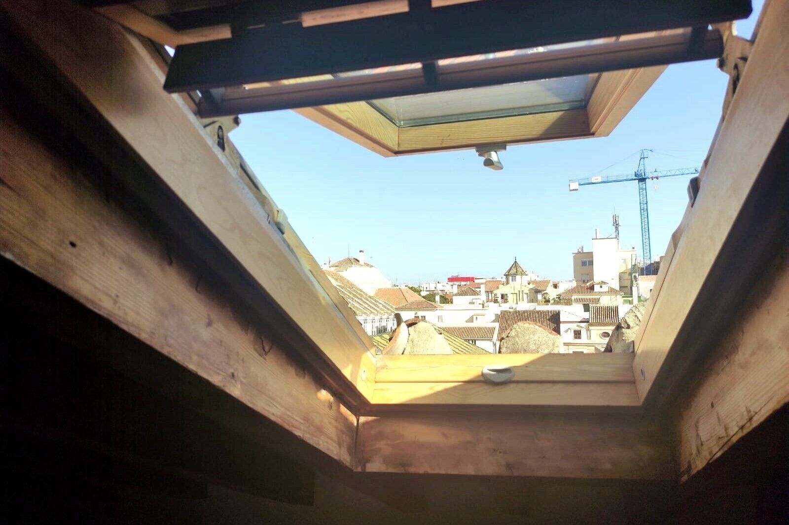 Een dakraam met uitzicht op een stadsbeeld, inclusief gebouwen en een kraan.