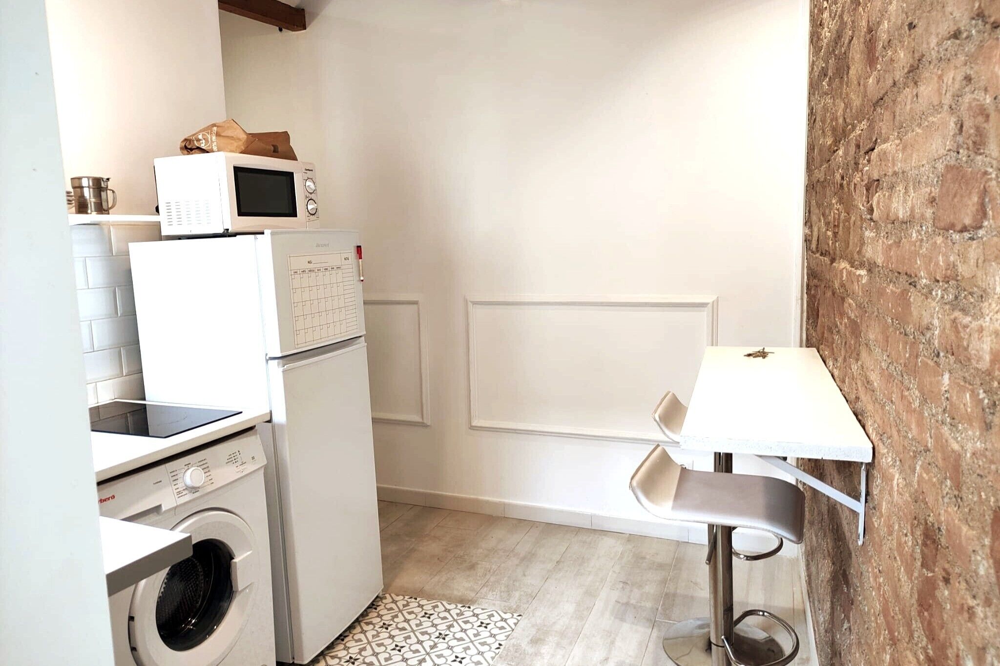 Cocina compacta con lavadora, microondas y una pequeña mesa con una silla.