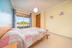 A bedroom with a bed, a window with curtains, a wooden door, and a ceiling light. - 1-Bedroom Apartment with Shared Pool, Wi-Fi and Air Conditioning (Armação de Pêra)