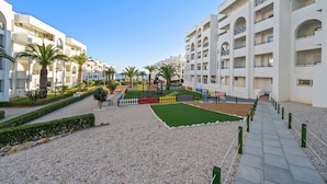 Un pati d'hotel amb un camí de grava, palmeres i una zona de jocs per a nens.
