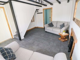 A room with a grey sofa, a wooden coffee table, a small table with a vase, a blue door, and a staircase with white walls and black beams.