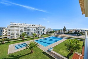A hotel with a swimming pool, palm trees, and a view of the sea. - 1-Bedroom Apartment with Shared Pool, Wi-Fi, and Air Conditioning (Armação de Pêra)