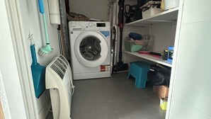 A laundry room with a washing machine, a fan, and shelves with various items. - Well-being apartment (Saint-Pée-sur-Nivelle)