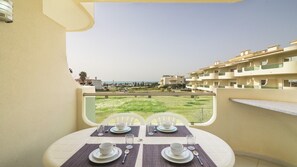 A balcony with a table set for two, overlooking a residential area and a body of water. - 1-Bedroom Apartment with Sea and Garden View (Armação de Pêra)