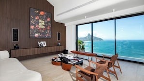 A modern living room with a large window overlooking the ocean, a sofa, a coffee table, and a wall-mounted speaker.