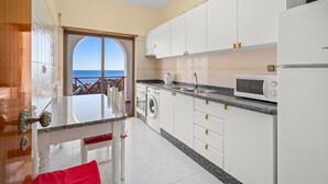 Cozinha com vista para o mar, armários brancos, máquina de lavar e micro-ondas.