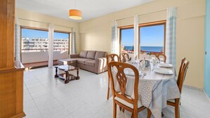 Uma área de refeições com mesa posta para quatro pessoas, um sofá e vista para o mar.