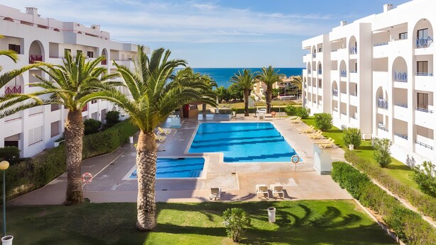 Resort com piscina, palmeiras e vista para o mar.