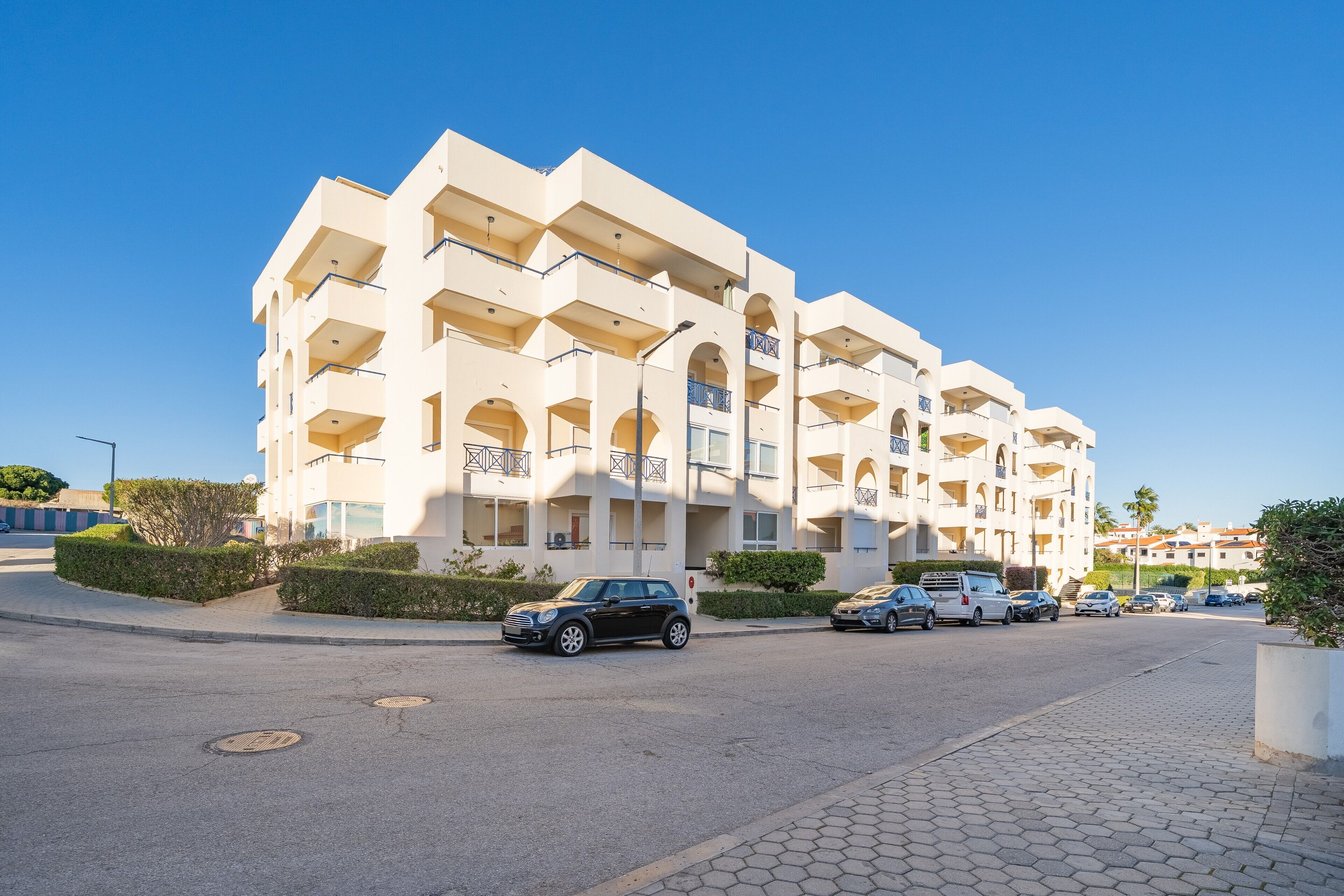 A multi-story hotel with balconies, a paved street, and parked cars.
