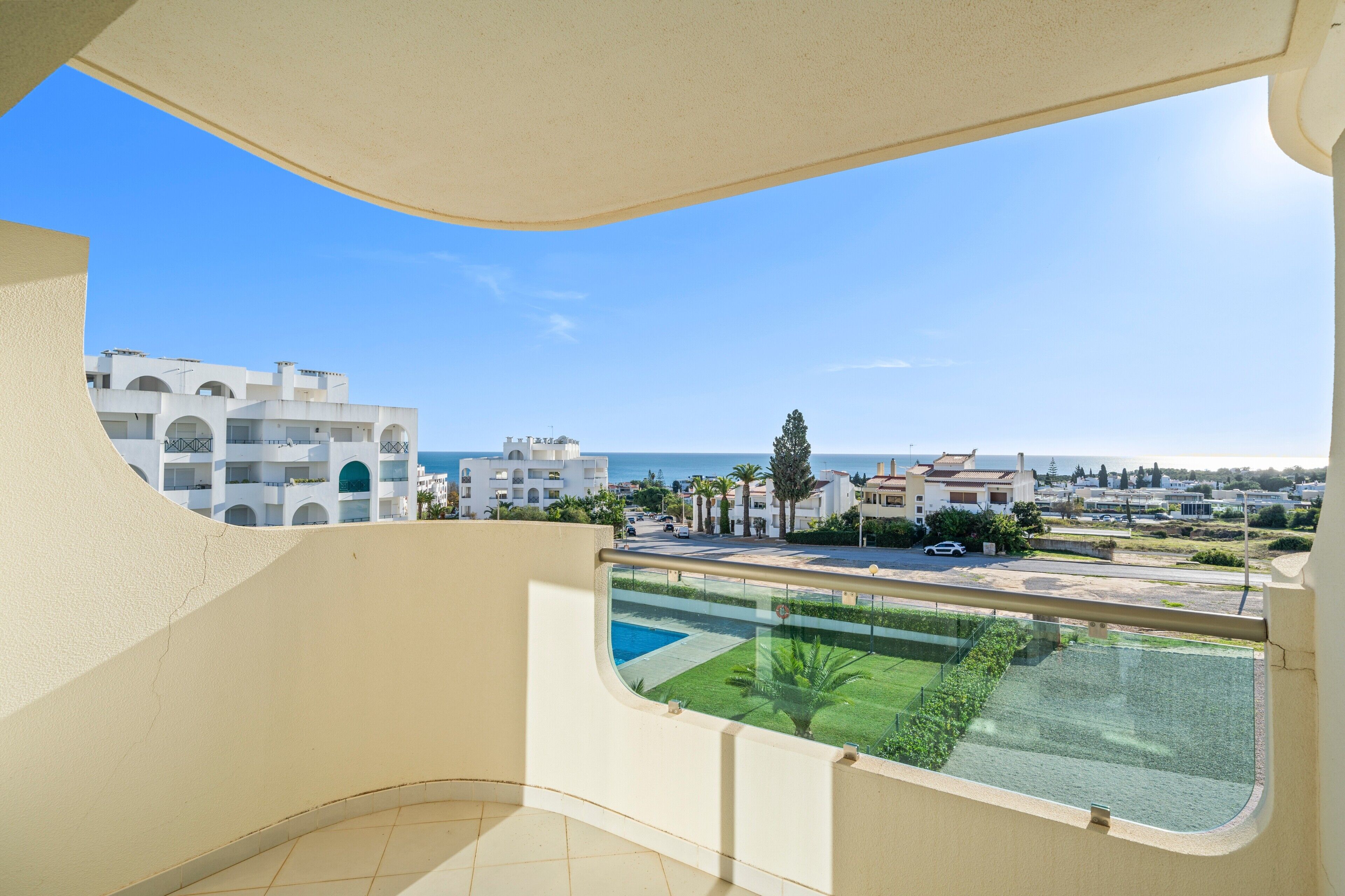 A balcony with a view of a residential area, a swimming pool, and the sea.