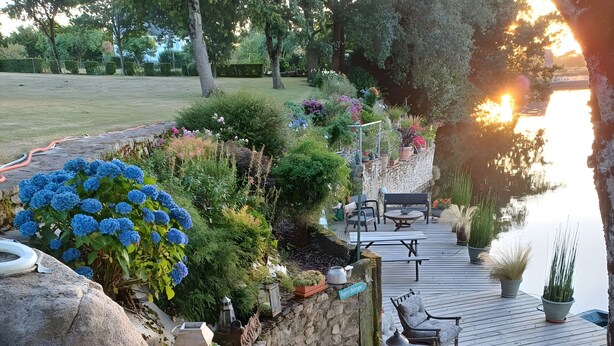 A garden patio with a stone wall, potted plants, and a view of a body of water. - Apartment "Le clos du pont" with Lake View, Shared Pool and Wi-Fi (THEIX-NOYALO)