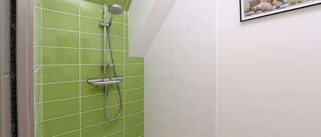 A bathroom with green and white tiled walls, a shower with a handheld showerhead, and a framed picture on the wall.