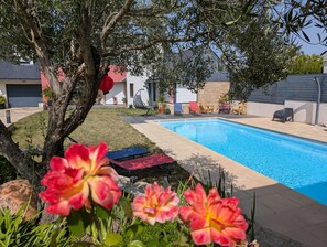 Un jardin avec une piscine, une chaise rouge et une chaise suspendue.