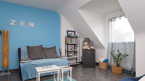 Una habitación con pared azul, un sofá, una mesita, un armario y una ventana con cortinas.