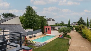 Un patio trasero residencial con piscina, un pequeño edificio rojo y un césped.
