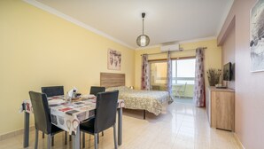 A room with a dining table, chairs, a bed, a TV, and a window with curtains. - Studio 'Sea View - 2 Rc C' with Sea View, Wi-Fi and Air Conditioning (Armação de Pêra)