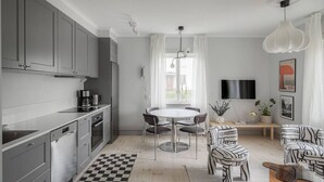 A modern kitchen with grey cabinets, a dining table with chairs, a coffee machine, and a TV mounted on the wall. - Stylish 2BR Apartment in Central Sundbyberg (Sundbyberg)