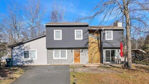 Une maison à deux étages, à l’extérieur gris, avec une porte d’entrée et un petit porche aménagé avec du mobilier d’extérieur.