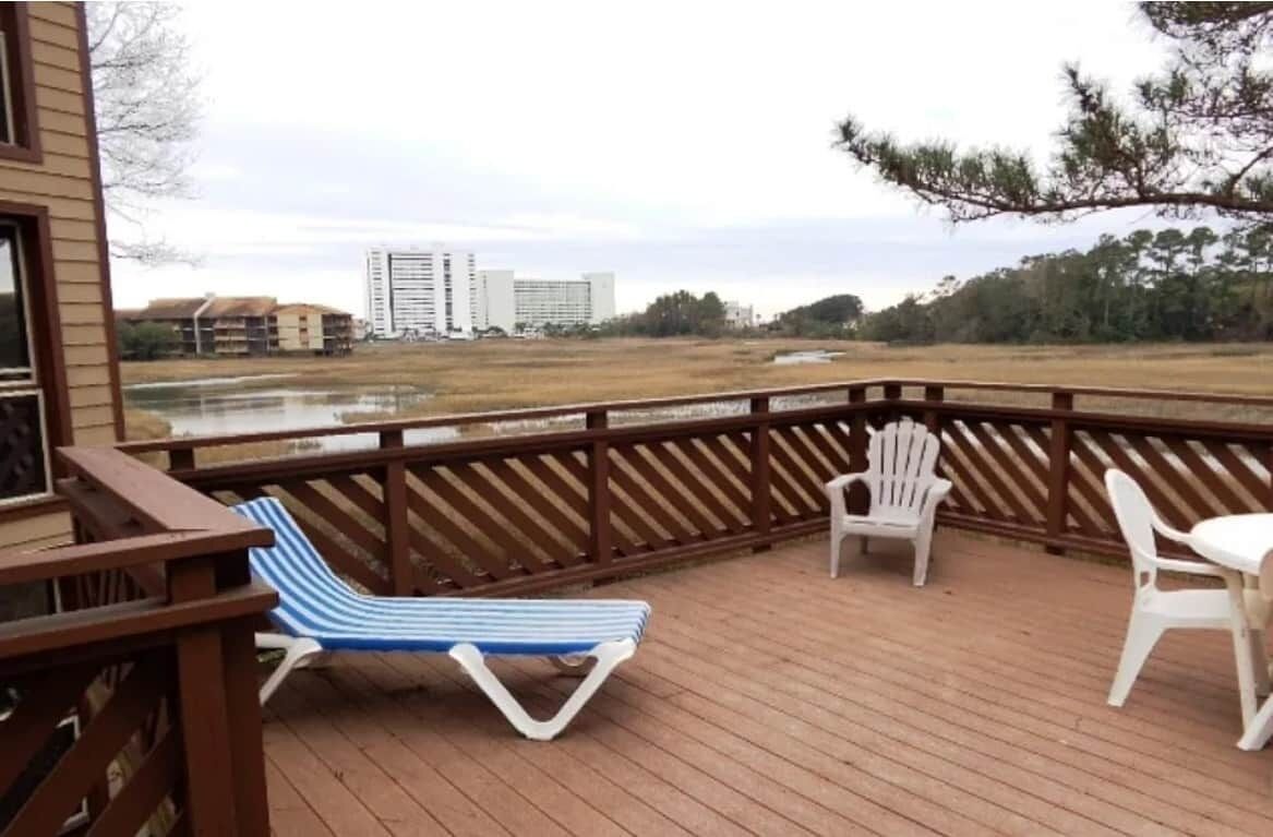 Una terraza de madera con vista a un cuerpo de agua y edificios a lo lejos.