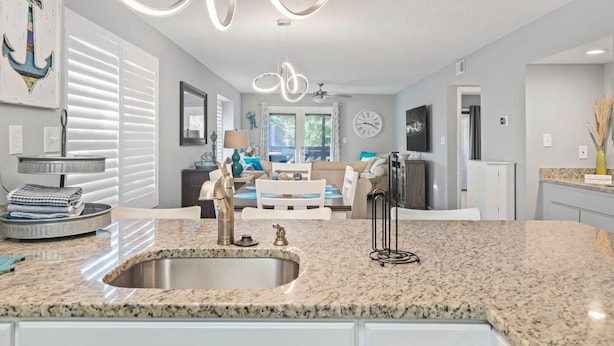 A modern kitchen with granite countertops, a stainless steel sink, and a dining area with a white table and chairs. - Waves & Rays - Stay, Play, and Soak Up the Day! (Horry County)