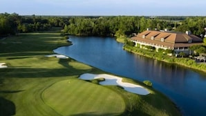A golf course with a large body of water, a clubhouse, and a well-maintained lawn. - Waves & Rays - Stay, Play, and Soak Up the Day! (Horry County)