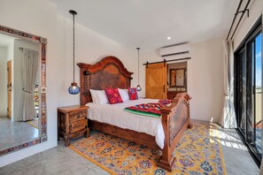 Une chambre spacieuse avec un grand lit, une tête de lit en bois, une table de chevet, un miroir et une vue sur l’extérieur.