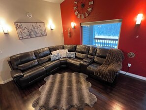 A living room with a sectional sofa, a rug, a wall clock, and a window with a view of a snowy deck. - Luxury 3 bedroom house in wonderful Fairbanks (Fairbanks)
