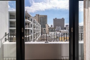 Uitzicht vanaf een balkon over een stadsgezicht met moderne gebouwen, een heldere lucht en een metalen hekwerk.